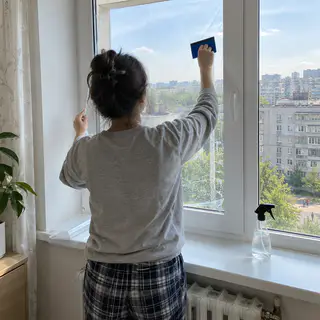 Людина клеїть захисну плівку на вікно квартири ракелем (ілюстрація)