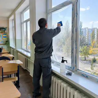 Монтажник клеит пленку на новое окно класса (иллюстрация)
