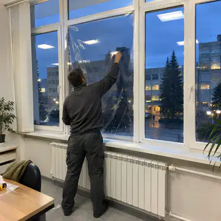 Монтажник клеїть плівку на скло офісу підприємства ввечері (ілюстрація)
